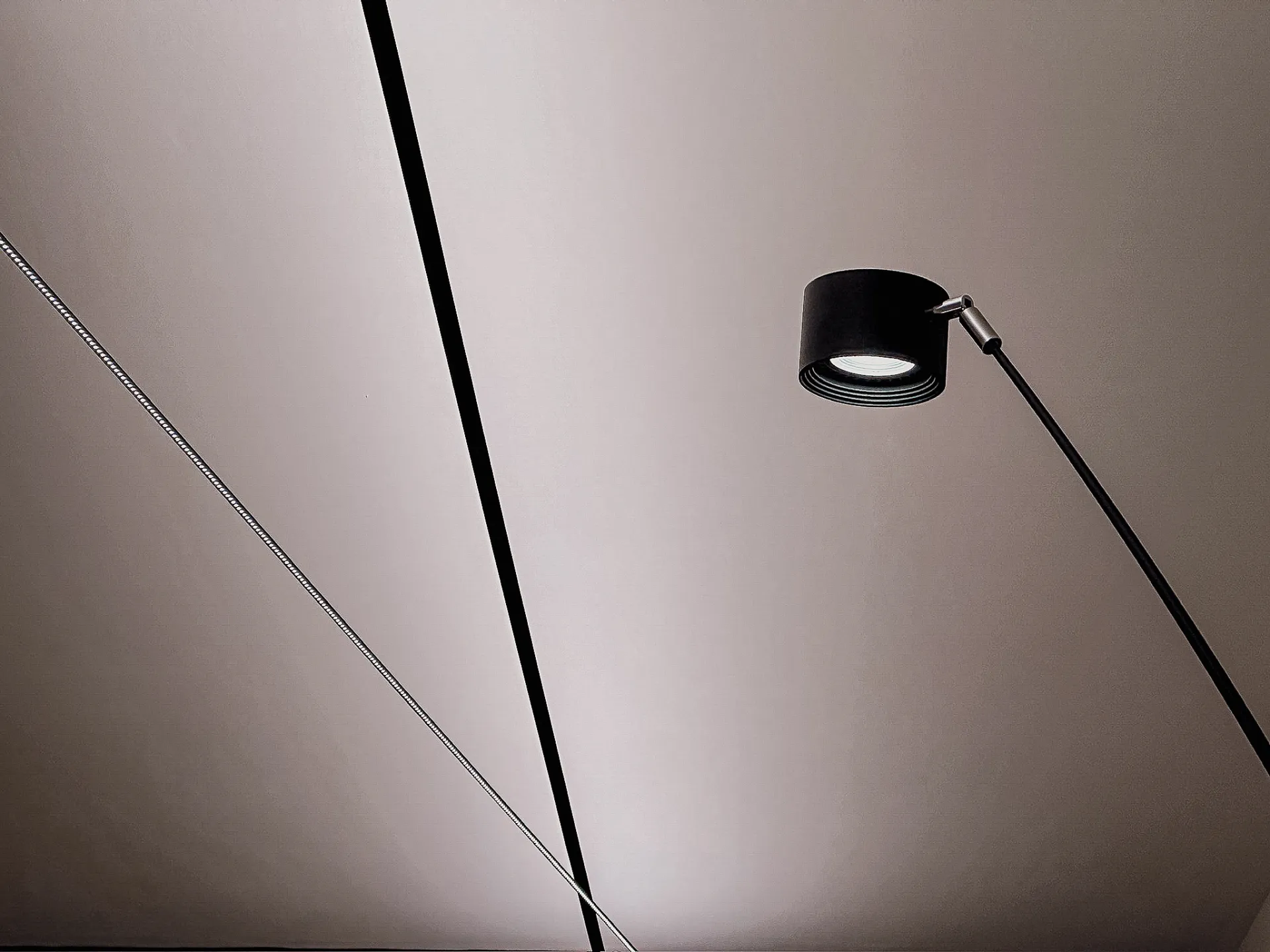 Un cavo teso e la testa di una lampada disegnano linee sottili nella penombra